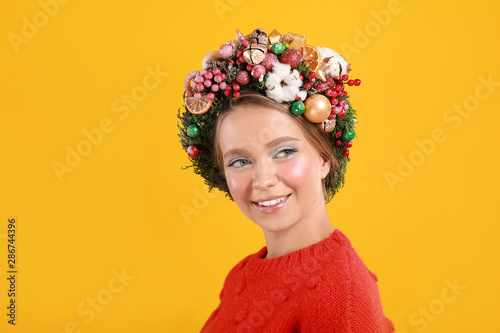 Beautiful young woman wearing Christmas wreath on yellow background