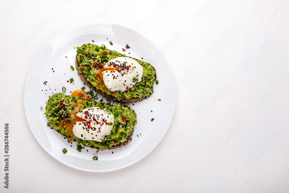 Poached eggs with avocado guacomole on brown bread with sesame seeds. Healthy breakfast on a white background. Copy space.