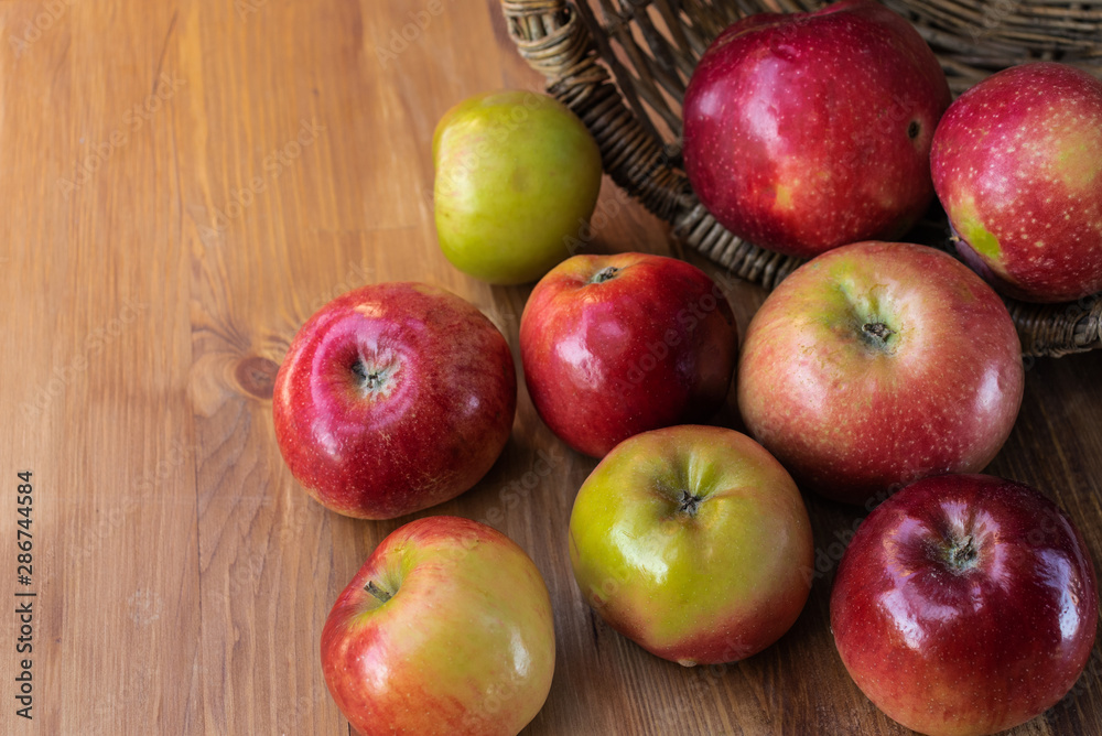 Red and green apples spilled out from a wicker basket lying on its side onto a brown wooden board, top side view Red and green apples spilled out from a wicker basket lying on its side onto a brown wooden board, top side view