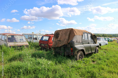 Vintage car cemetery in a field under blue sky with clouds photo