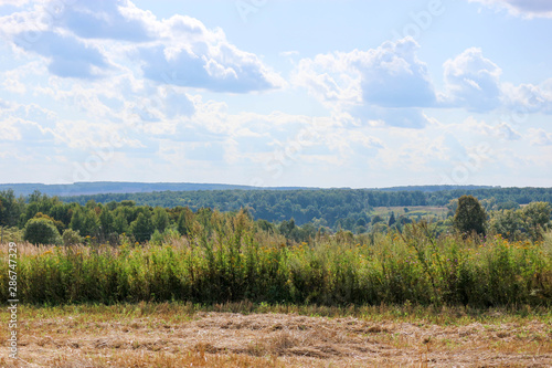 russian landscape with sloping field, hills, blue sky and clouds