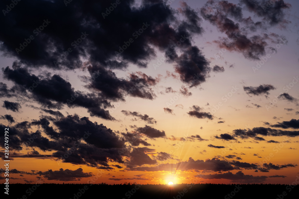 Evening sky at sunset background. Dark clouds hanging above horizon. Majestic cloudscape in blue, orange, violet shades. Grey cloudlets bringing rain. Countryside skyline in twilight time