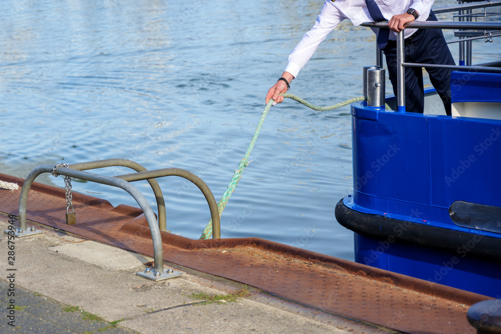 Naklejka premium captain or helmsman attaches the boat to the harbor quay with a rope, copy space