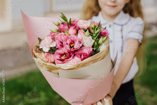Fototapeta Naklejka Na Ścianę i Meble -  School girl dressed in school uniform holding a bright pink festive bouquet of beautiful flowers for teacher. No face. Blurred background.