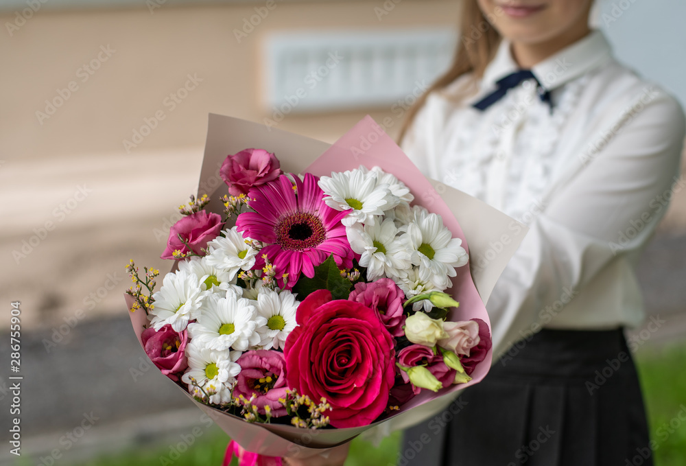 School girl dressed in school uniform holding a bright pink festive bouquet of beautiful flowers for teacher. No face. Blurred background. School girl dressed in school uniform holding a bright pink festive bouquet of beautiful flowers for teacher. No face. Blurred background.