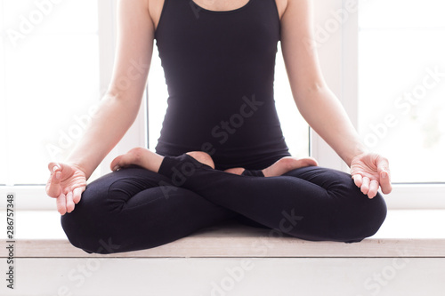 Blond woman in sport outfit sits on windowsill in lotus pose