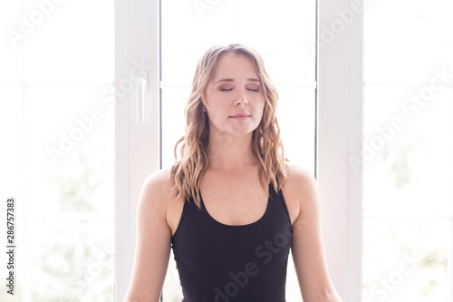 Blond longhaired girl doing meditating exercises near window
