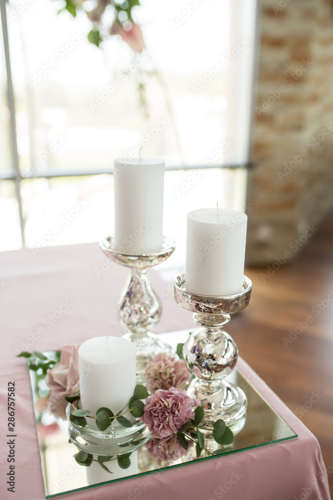 The wedding table setting for the newlyweds is decorated with fresh flowers of carnation, rose, anthurium and eucalyptus leaves. Silver candlesticks, white candles. Wedding floristry. Closeup details The wedding table setting for the newlyweds is decorated with fresh flowers of carnation, rose, anthurium and eucalyptus leaves. Silver candlesticks, white candles. Wedding floristry. Closeup details