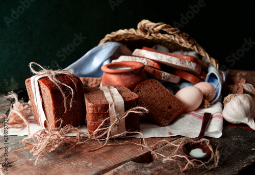 Black bread slices wrapped with white paper and tustic thread with a pot of milk, eggs and garlic on a white towel. photo