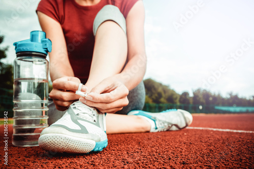 She is tying shoelaces. Athlete girl at a stadium with a bottle of water. Concept of fitness and sport.