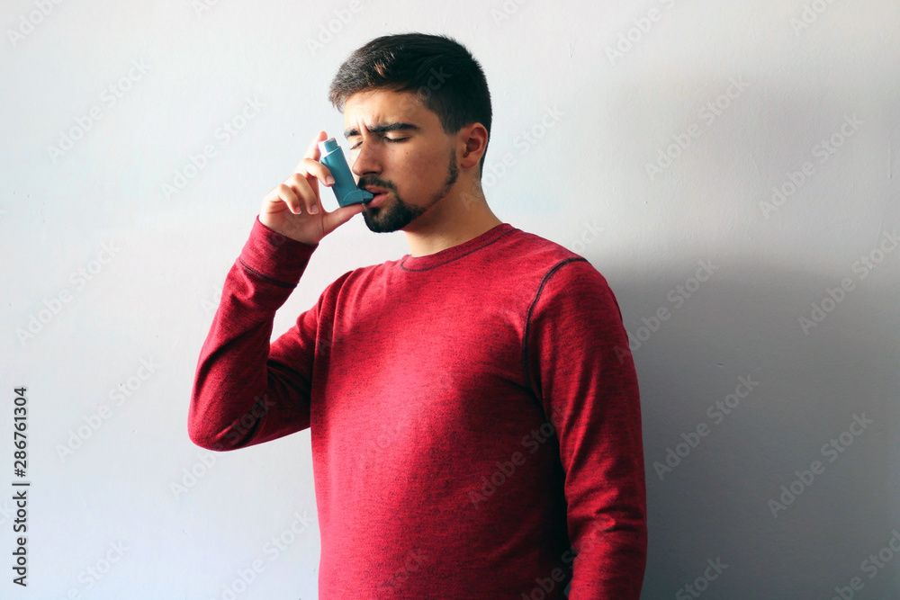 Health and medicine - Young man using blue asthma inhaler to prevent an asthma attack. Health and medicine - Young man using blue asthma inhaler to prevent an asthma attack.