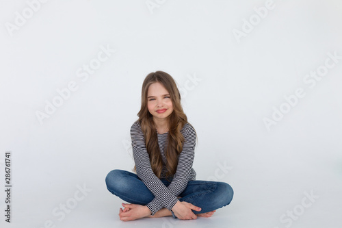 Yong funny girl sitting on the white floor - isolated over a white background