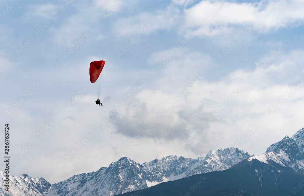 Two people flying with a Tandem and enjoying the freedom, high up in the sky with a few clouds and mountains covered in snow in the background