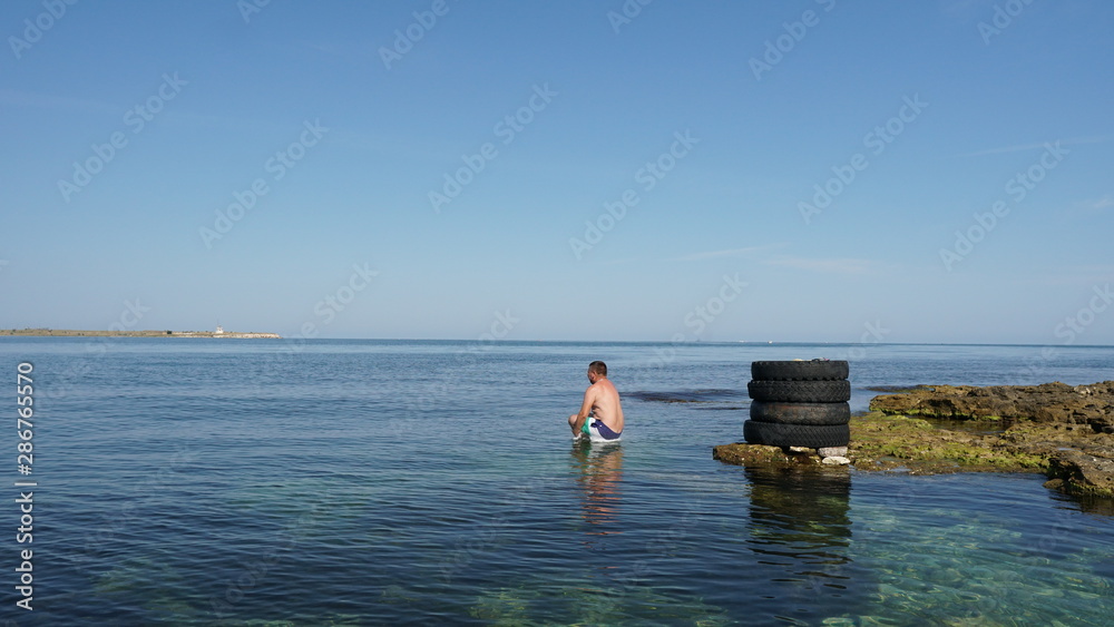 Brave man jumping to the deep blue sea from old tires on the coast. Brave man jumping to the deep blue sea from old tires on the coast.