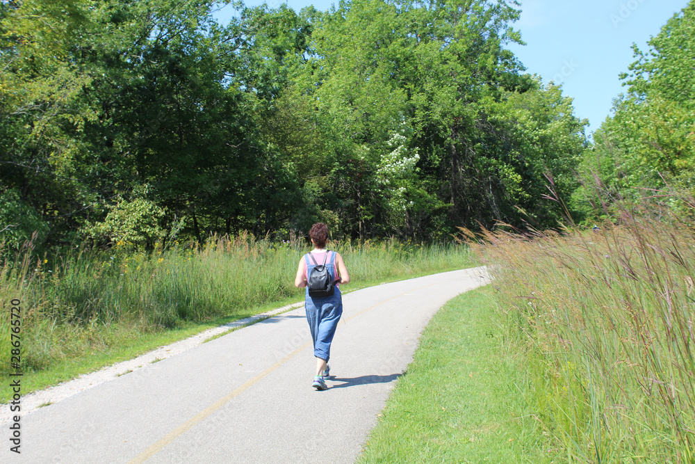 Woman with a backpack walking on the North Branch Trail at Bunker Hill Woods in Chicago Woman with a backpack walking on the North Branch Trail at Bunker Hill Woods in Chicago