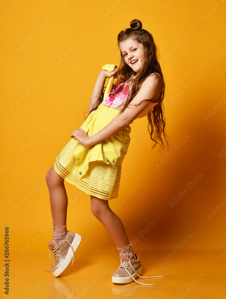 Full length portrait of a cute little teen girl in a stylish skirt and jacket clothes looking at the camera and smiling against a yellow studio wall. Full length portrait of a cute little teen girl in a stylish skirt and jacket clothes looking at the camera and smiling against a yellow studio wall.