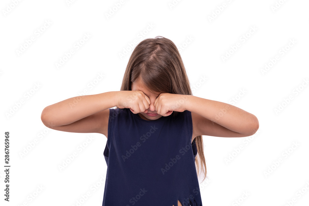 Little girl rubs her eyes and cries on a white background.