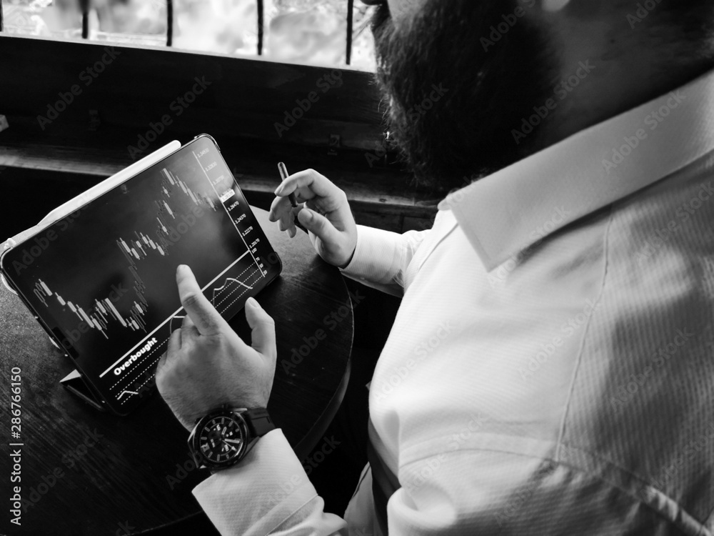 bearded adult rich businessman checking stock market for-ex on his pro tablet with smart watch black and white