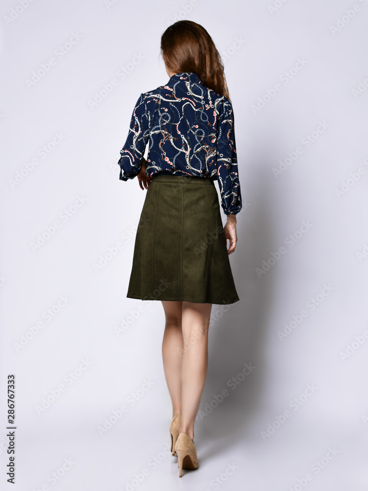 Woman back in a blue silk blouse with floral patterns, a dark short skirt with buttons and high-heeled shoes Woman back in a blue silk blouse with floral patterns, a dark short skirt with buttons and high-heeled shoes