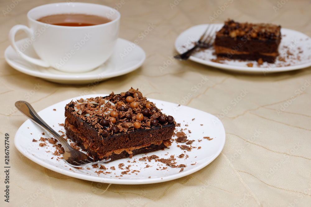 Chocolate cake and tea. Two pieces of sponge cake on a white plate and a white cup with tea Chocolate cake and tea. Two pieces of sponge cake on a white plate and a white cup with tea