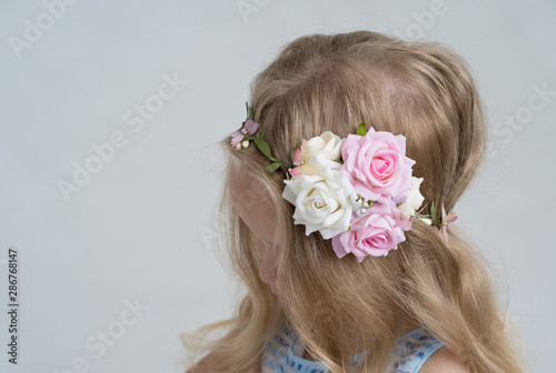 Litte blond girl with a flower crown. Side view, no face, on the white background, white and pink roses in her hair.