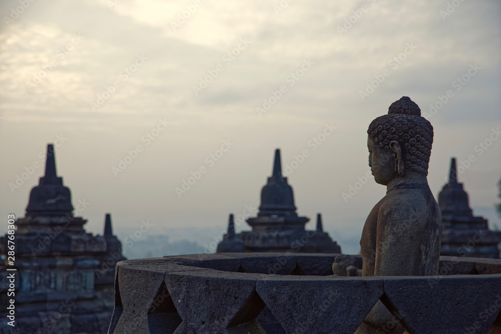 Java, Indonesia - July 24, 2019: Amazing sunrise view of meditating Buddha statue and stone stupas. Ancient Borobudur Buddhist temple. Great religious architecture