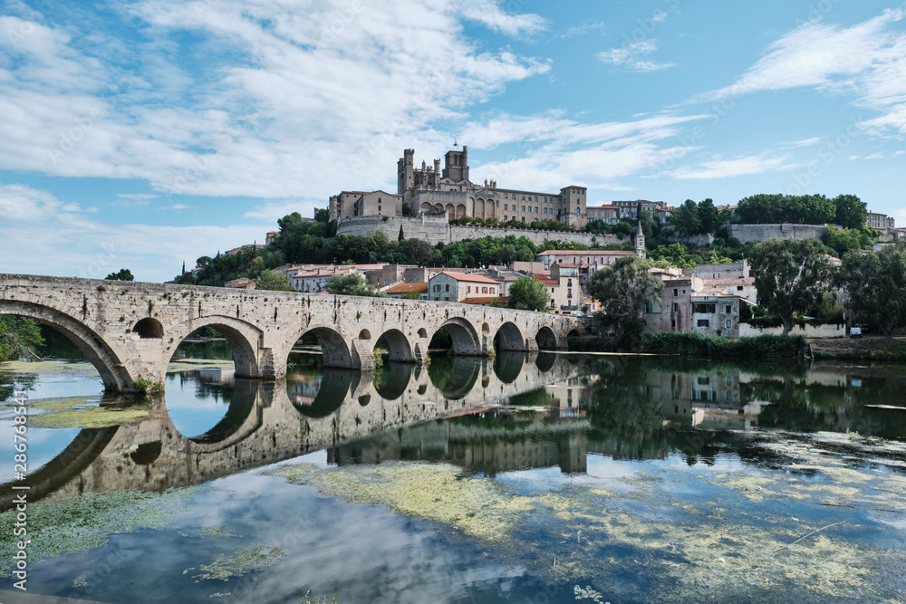The old Roman Bridge and the city of Beziers in France reflected in the waters of the River Orb
