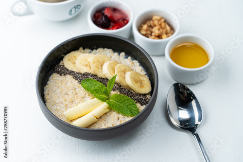 Healthy sweet breakfast with whole grain porridge  chia seeds  butter  banana and other toppings  served with a cup of black coffee on a white background