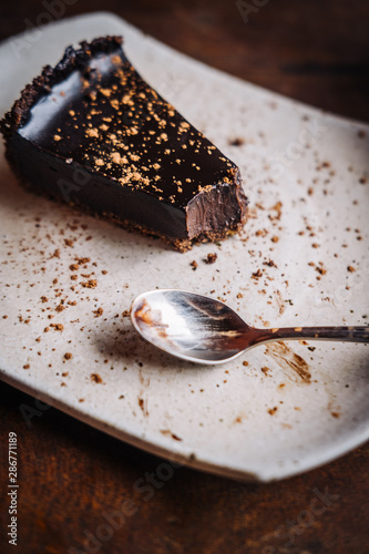 Slice of raw vegan rich dark chocolate cake on a white plate at restaurant. Closeup, minimalism food photograohy concept photo