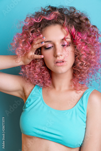 Portrait of beautiful woman with pink curly colored hairs in blue swimsuit. Glitter makeup. 90s style. Ombre. Isolated on blue