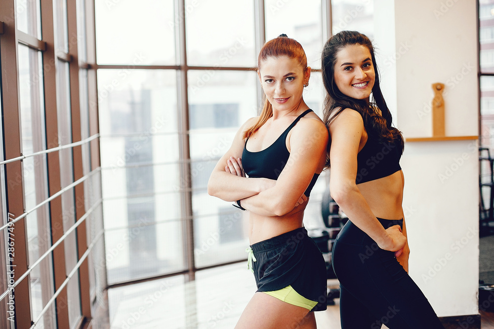Obraz premium Beautiful girls in the gym. A women performs exercises. Brunette in black form