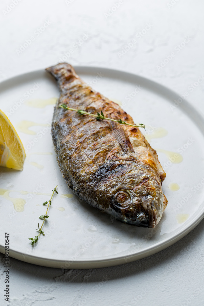 Dorado on grill with lemon on white concrete table Dorado on grill with lemon on white concrete table
