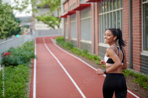 Stunning young black woman, fitness model, works out on outdoor track - jogging