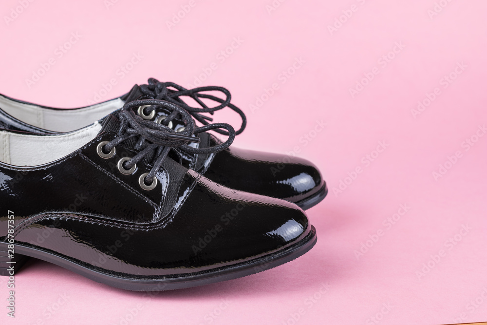 A pair of fashionable black women's shoes on a pink background.