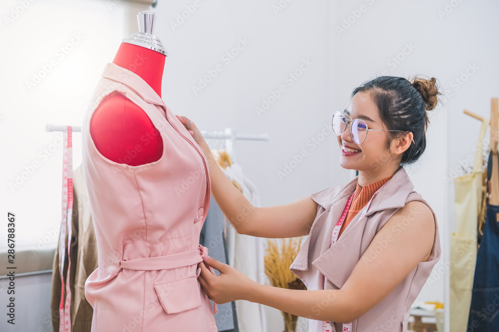 Happy Asian female fashion designer girl making fit on the formal dress uniform clothes on mannequin model. Fashion designer stylish showroom. Sewing and tailor concept. Creative dressmaker stylist. P...
