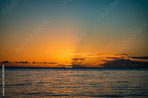 Low clouds block a small bit of sun as it passes below the horizon on a calm ocean at Anaeho omalu Beach on the Big Island of Hawaii