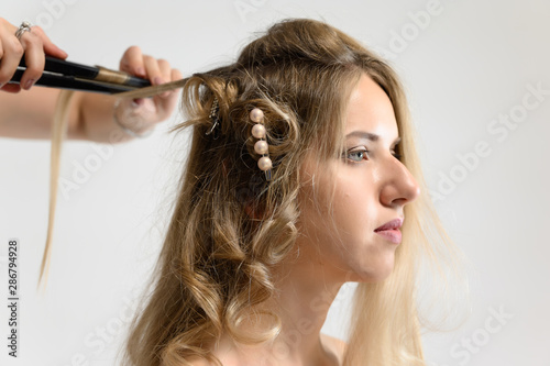 A photo of a hairdresser working on a model's hair in a studio. Makes a hairstyle, styling hair on a white background.