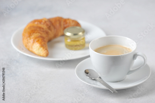 Coffee with croissant on a light background. Near the croissant a jar of honey. Close-up. Free space for text.