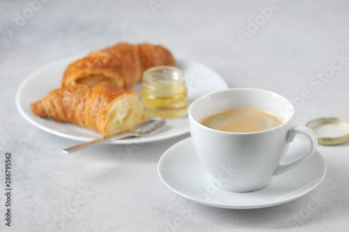 Coffee with croissant on a light background. Near the croissant a jar of honey. Close-up. Free space for text.