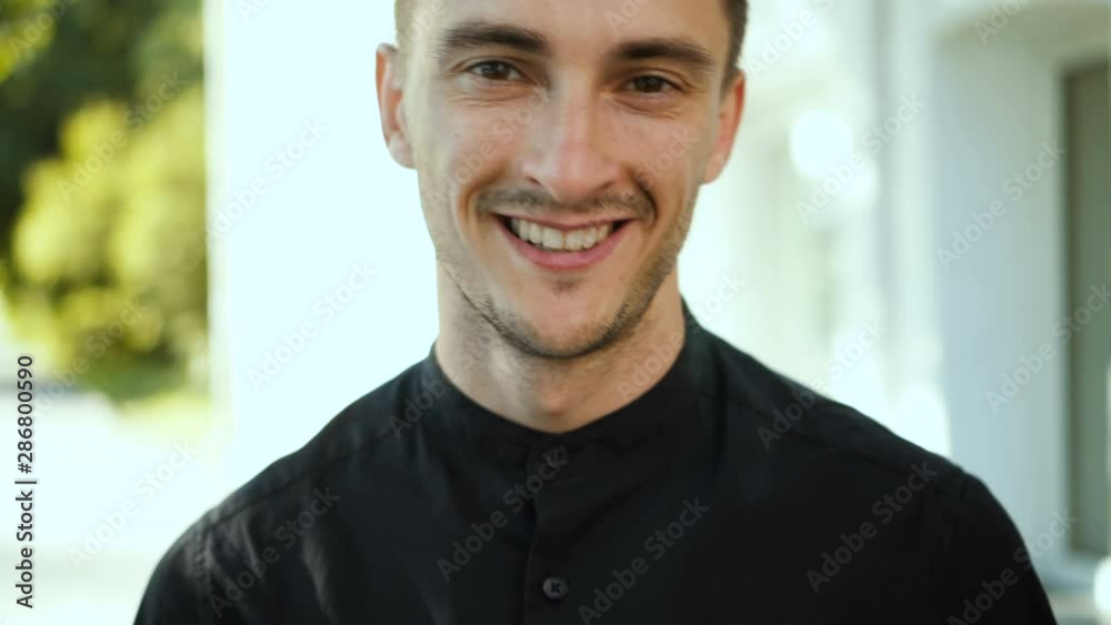 Handsome smiling young man portrait. Cheerful man looking at camera standing outdoors. Close up Handsome smiling young man portrait. Cheerful man looking at camera standing outdoors. Close up