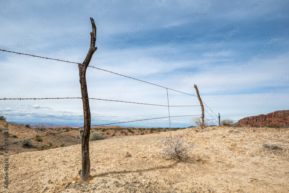 USA, Nevada, Clark County, Gold Butte National Monument. Barb wire fence strung on old wooden posts vanishing over a yellow gypsum hill.  This fence is for a grazing allotment for a Western cattle ran