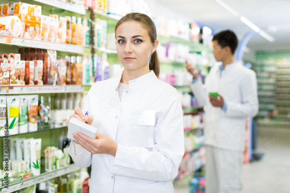 Woman is checking medicine with notebook in shelves in apothecary