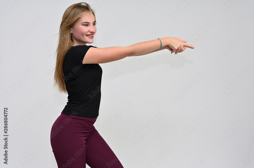 A knee-length portrait of a pretty brunette girl with long flowing hair in a black T-shirt and burgundy trousers on a white background. Smiling, showing emotions. A knee-length portrait of a pretty brunette girl with long flowing hair in a black T-shirt and burgundy trousers on a white background. Smiling, showing emotions.