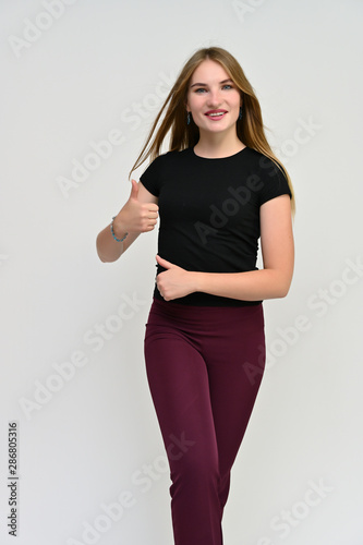 Full-length vertical portrait of a pretty brunette girl with long flowing hair in a black t-shirt and burgundy trousers on a white background. Smiling, showing emotions. © Вячеслав Чичаев