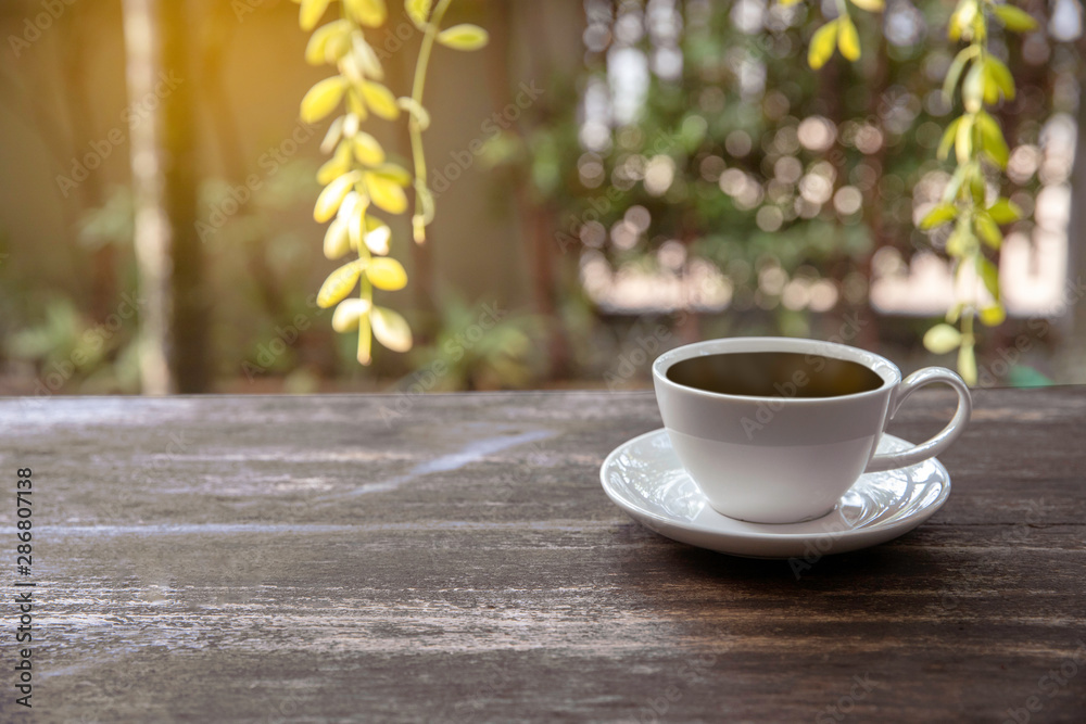 Fototapeta premium Hot cup of coffee on wooden tabletop on blurred green nature bokeh background