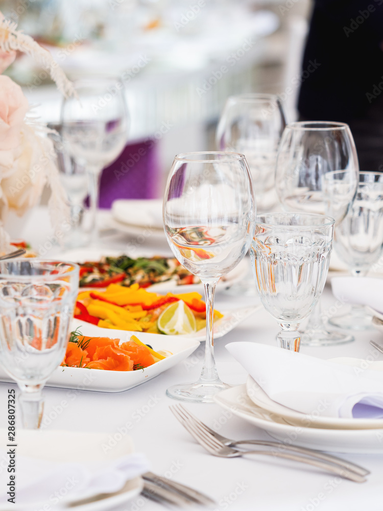 Table served for wedding banquet with cutlery and flowers in vases. Pastel colored decorations.