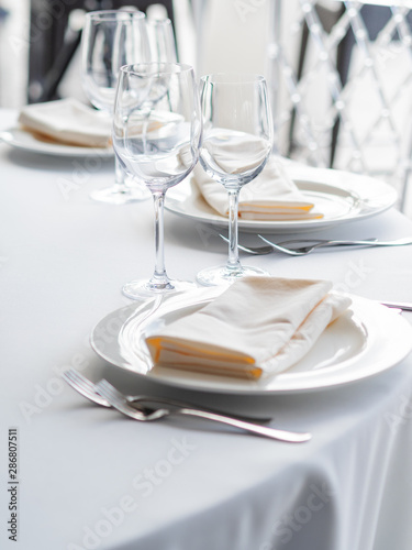 Table served for banquet with cutlery, wine glasses and napkins. Pastel colored decorations.