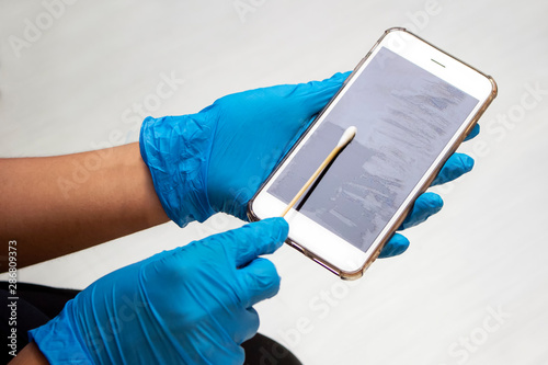 Hand holding cotton swab stick and swab dipped in diluted rubbing alcohol on screen of smartphone. Cleaning dirty screen phone for disease prevention from bacteria. Swap test device in laboratory.