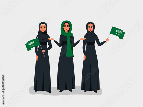 Happy Saudi women celebrate the Independence Day of the Kingdom of Saudi Arabia. Muslim girls dressed in black Abaya hold the KSA flags on the national day-September 23.