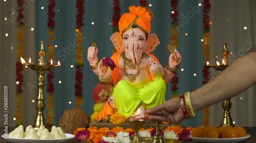 Shot of an Indian female's hand lighting up a diya / lamp for puja of Lord Ganesh Ji . Young female lighting up a lamp kept in front of decorated lord's idol - Indian festival for Hindus - Ganesh C... photo